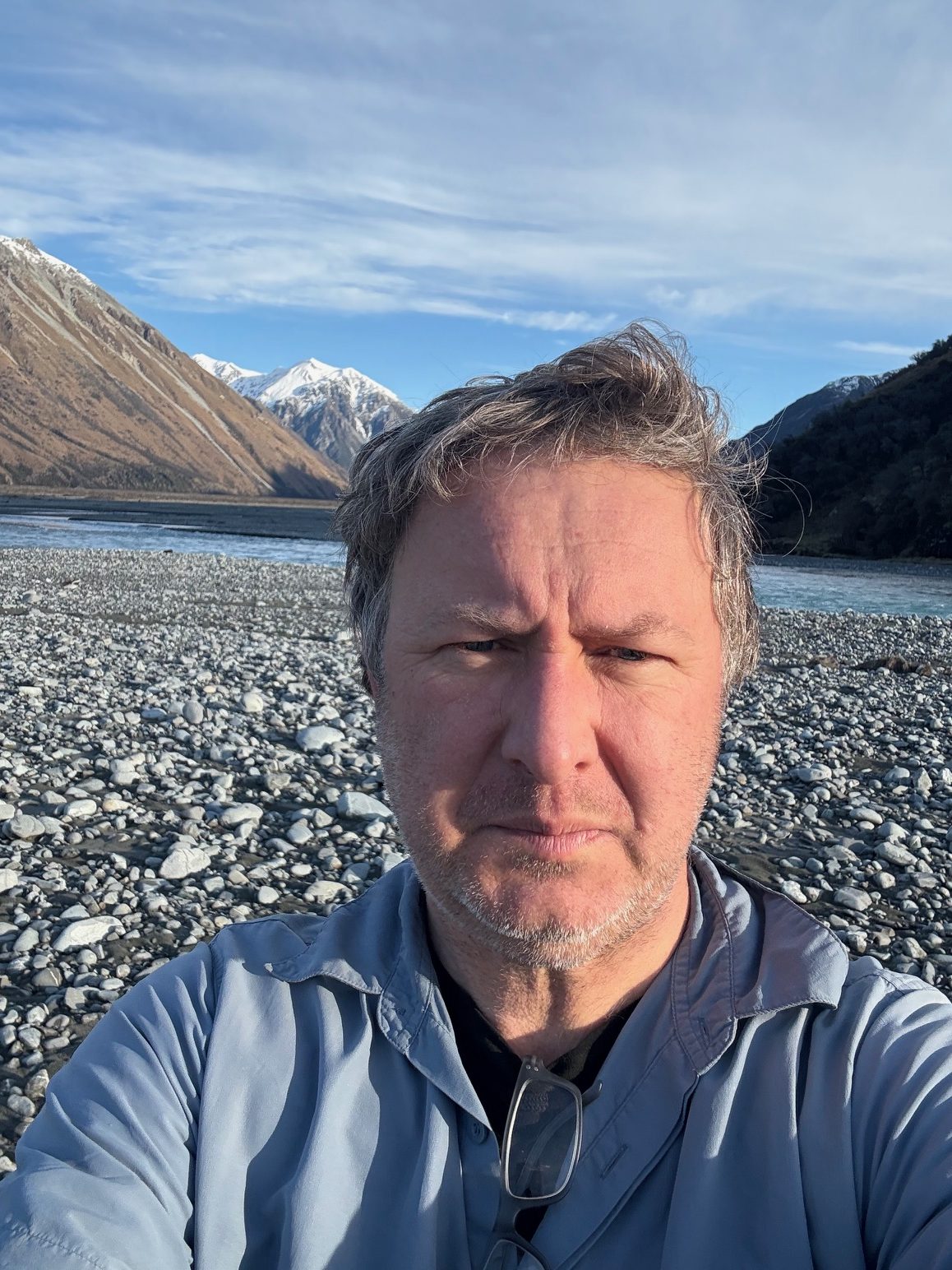A front on photo of poet Richard Reeve on a stony beach with mountains behind